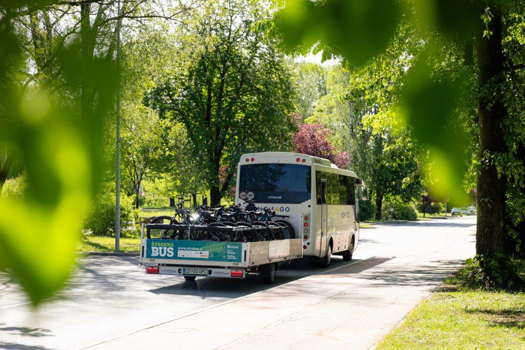 Štrekna bus se pelje po cesti s prikolico na kateri so naložena kolesa.