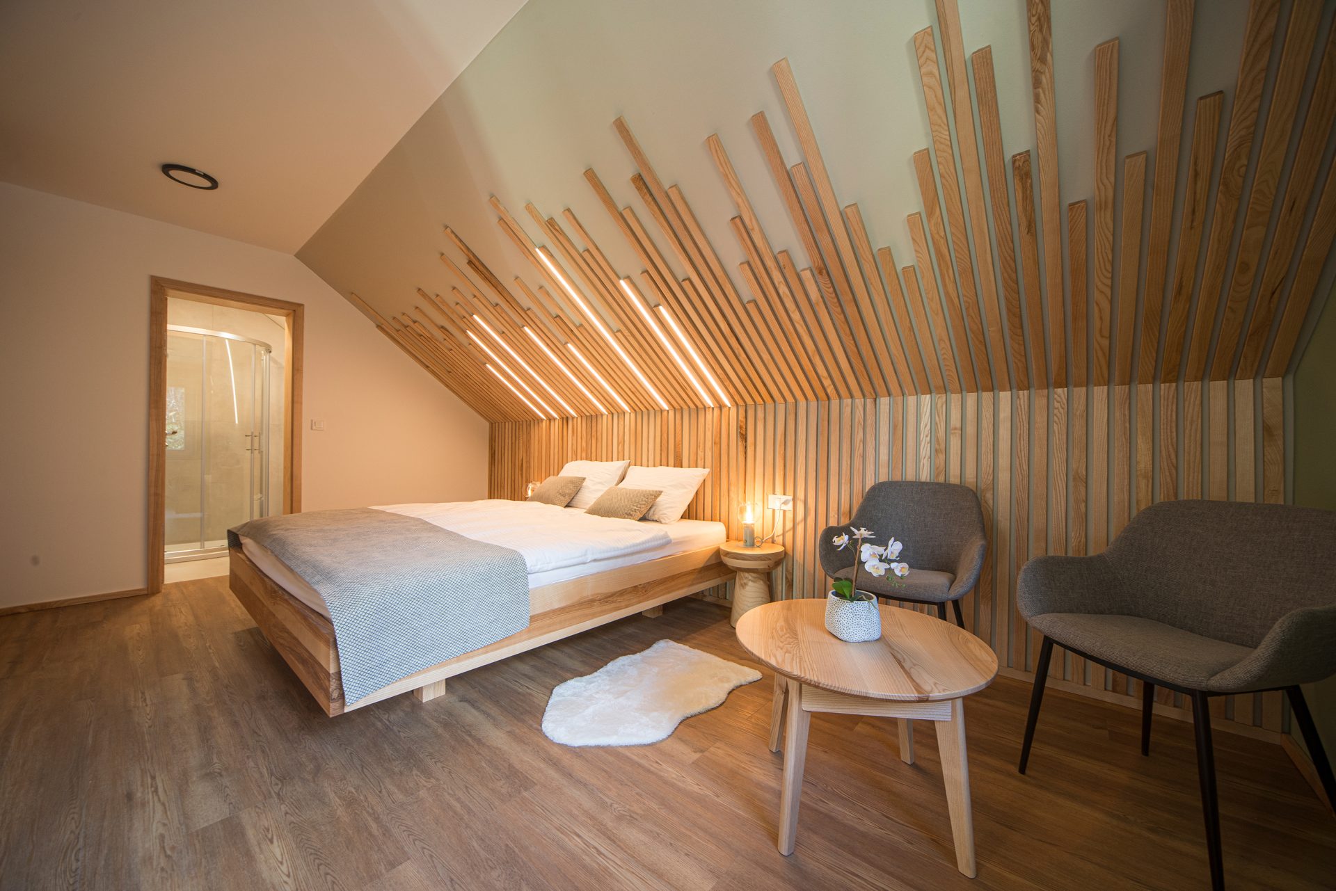 A modernly furnished room with wooden wall cladding and a comfortable sleeping nook with a small seating area.