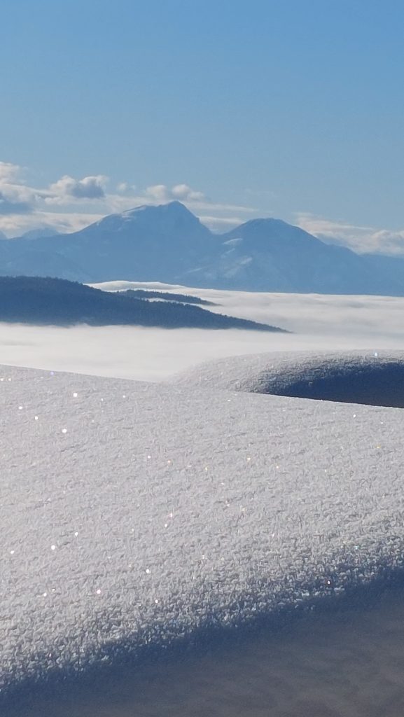 A view above Dravograd, where the winter landscape opens towards the snow-covered Koroška peaks and a sea of fog in the valleys.