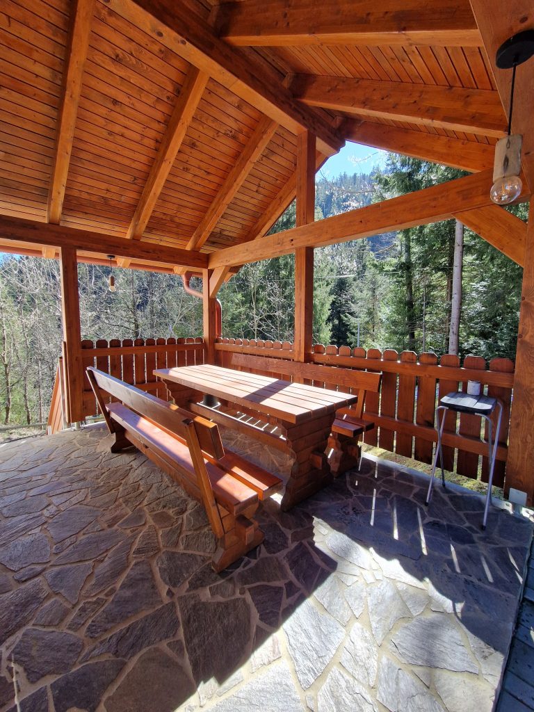 A spacious wooden terrace with a canopy, a solid wooden table, and benches.