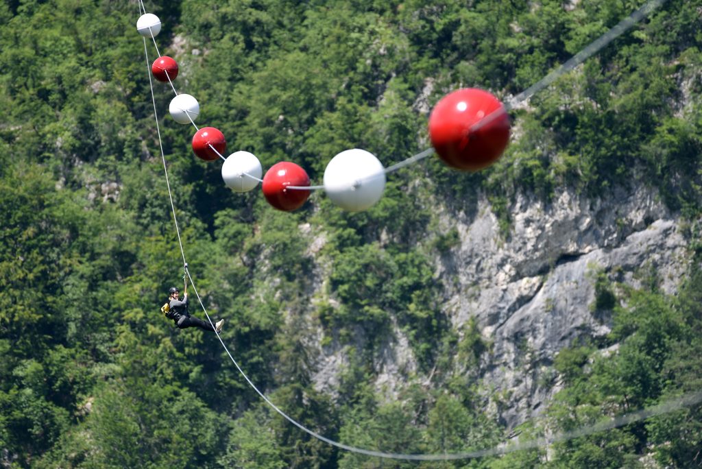On the Olimpline, a visitor descends high above the valley on a zip-line, surrounded by mighty rock faces and green forest.