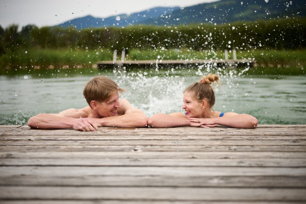 Two visitors enjoy refreshment and relaxed socializing in the natural swimming area and green surroundings.