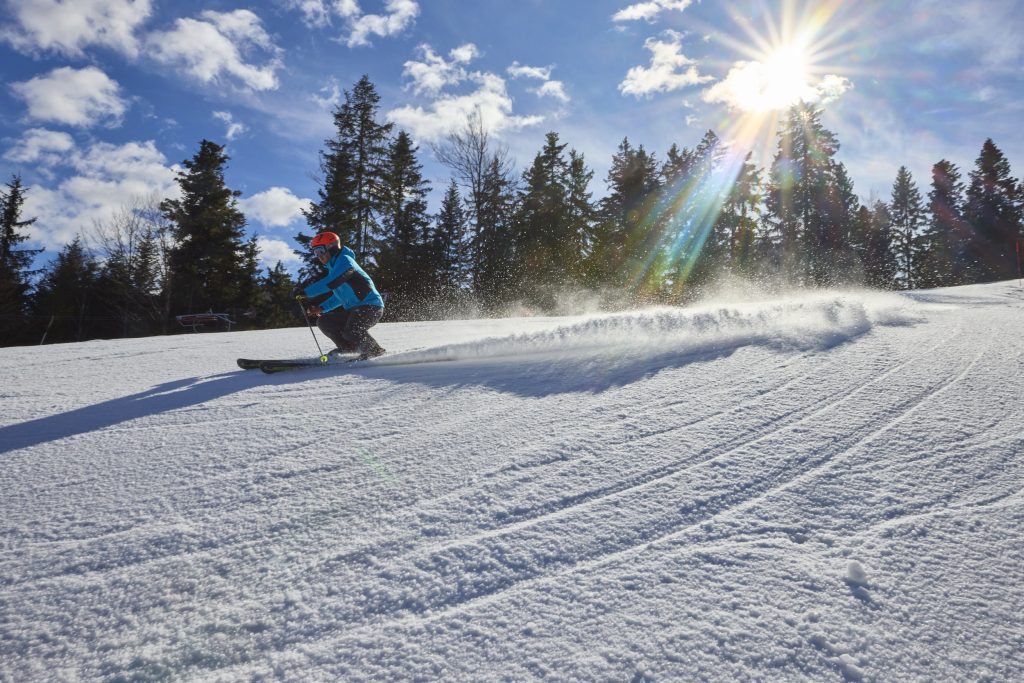A skier making a dynamic turn on well-groomed ski slopes.