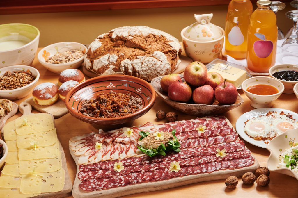 A richly laden table with homemade delicacies – fresh bread, cold cuts, cheeses, eggs, jams, and juices for an authentic farm indulgence.