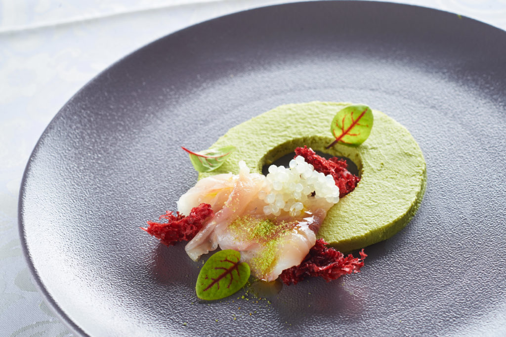 An elegant dessert in green tones, adorned with delicate leaves and white and red decorative accents.