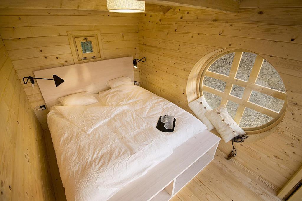 The interior of a wooden glamping hut featuring a cozy bedroom in warm natural tones with a large bed and a characteristic round window.