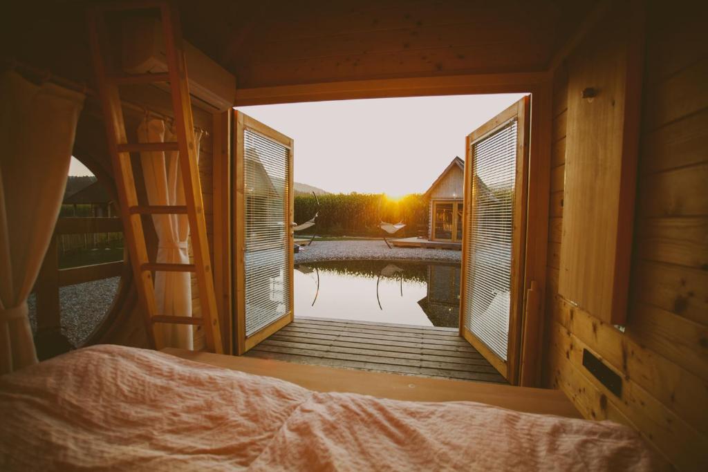 From the shelter of a wooden glamping hut, an idyllic view opens up to the natural swimming pool and surrounding greenery.