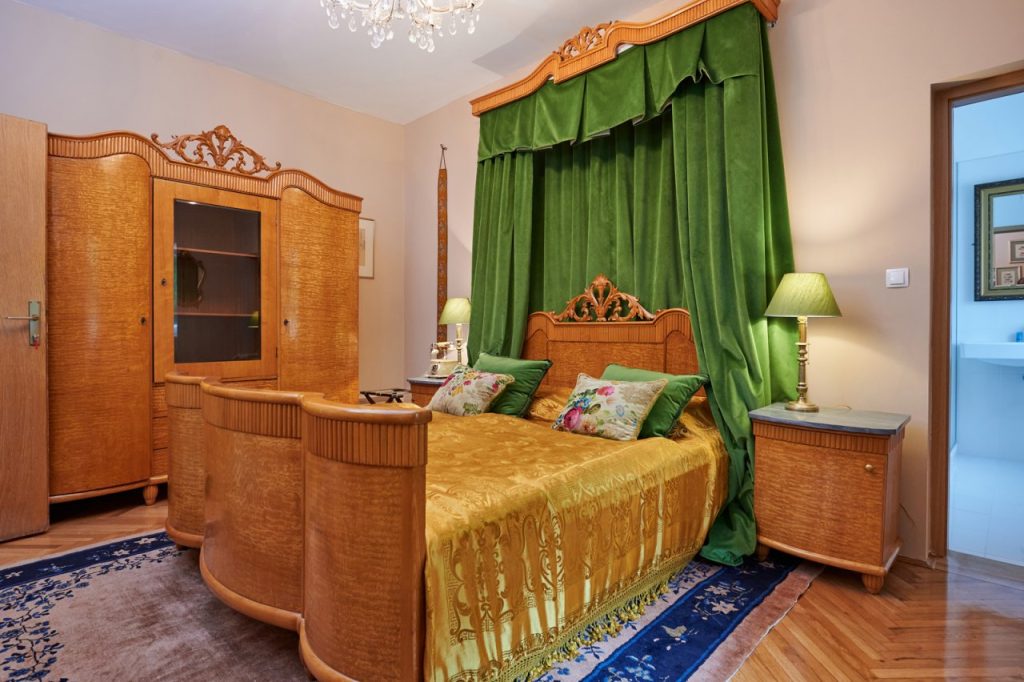 An elegantly furnished room with richly designed wooden furniture, a green canopy, and a touch of former castle comfort.