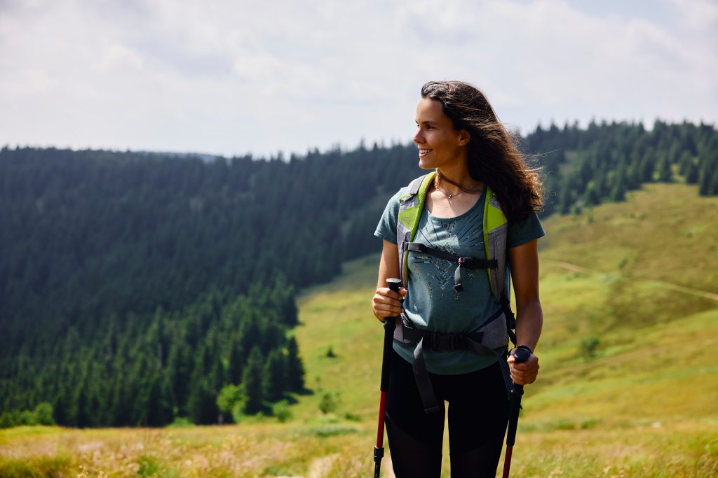 A hiker amidst green meadows and forested slopes.