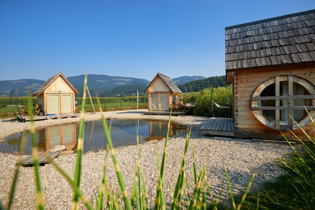 Green Resort glamping by the water park – wooden mill cottages set by a small water feature and surrounded by lush nature.