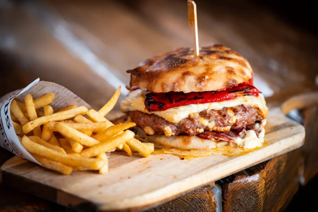 Sočen burger s sirom in pečeno papriko, postrežen s hrustljavim krompirčkom.