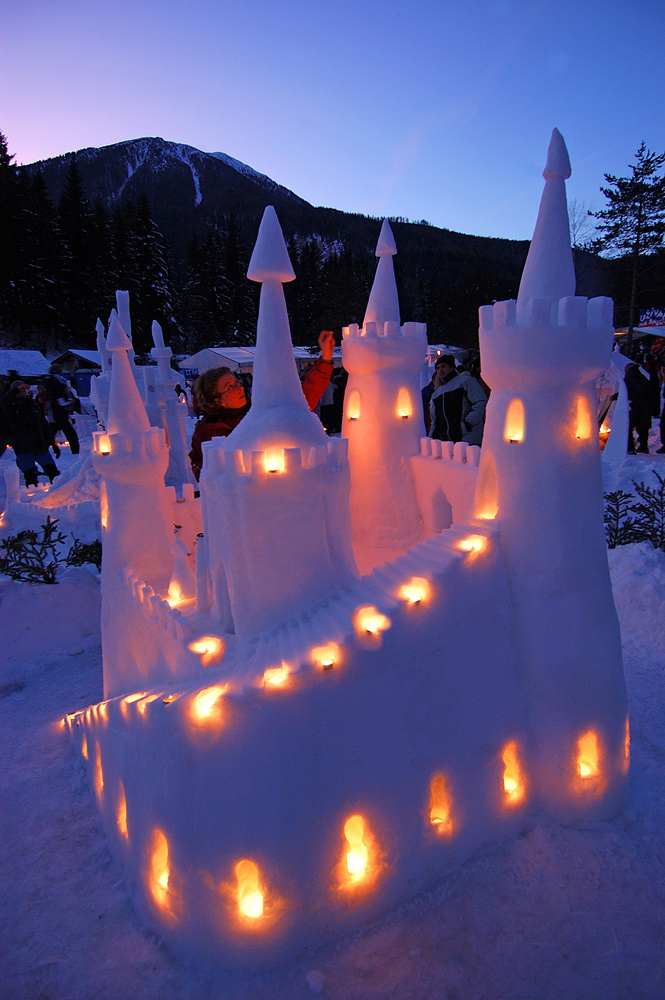 Snow castles glow in the evening in the magical light of candles.