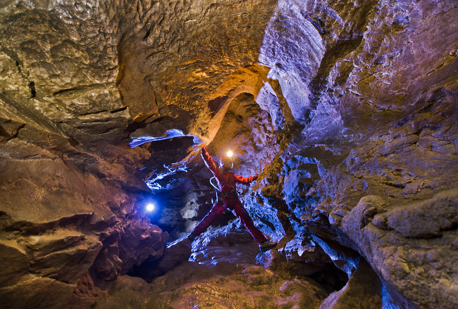 A visitor with a headlamp while climbing through the rocky cave landscape.