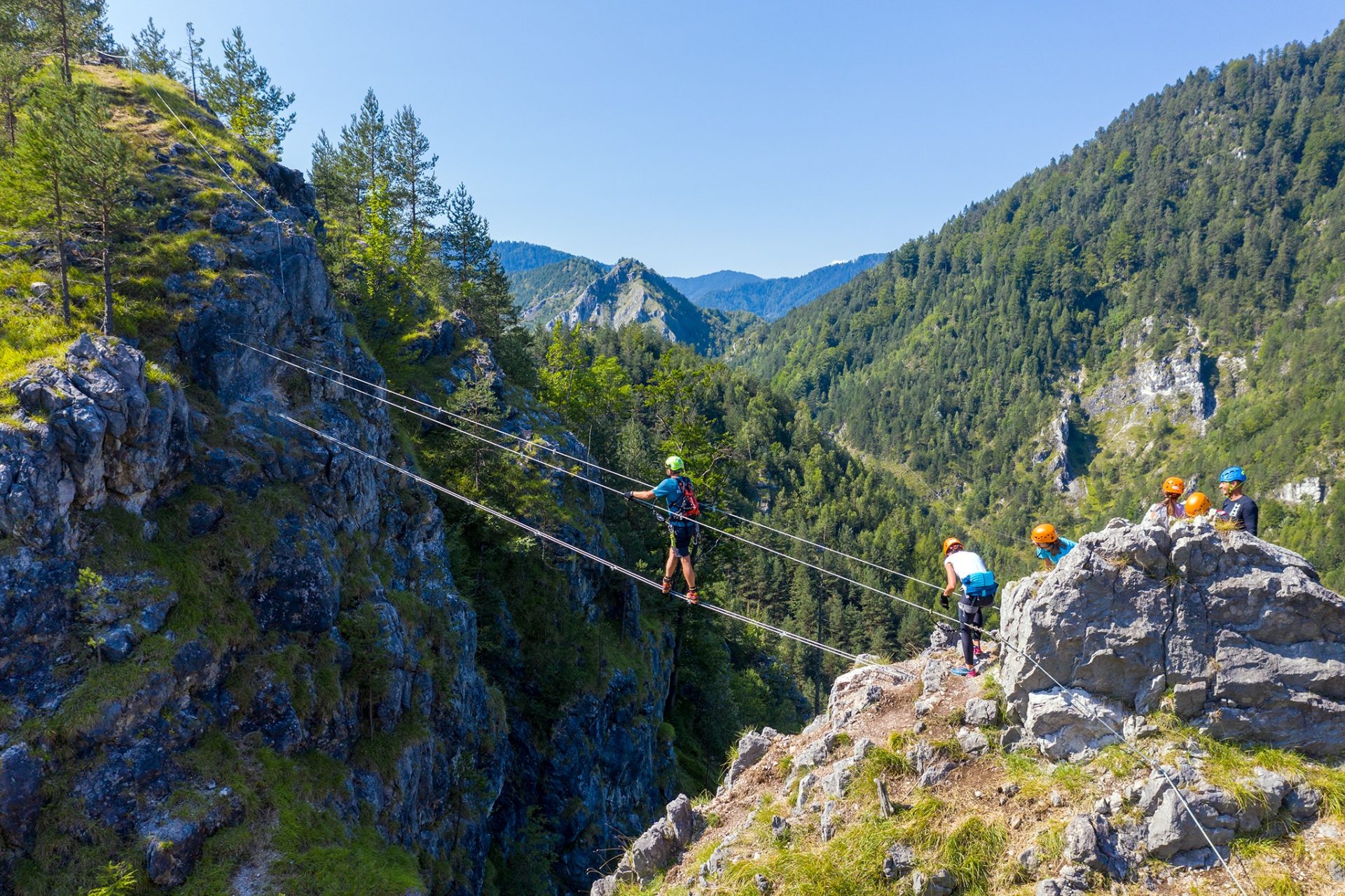 A group of climbers crossing the via ferrata on suspension bridges made of steel cables.