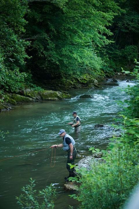 Two fishermen stand knee-deep in the river, trying their luck.