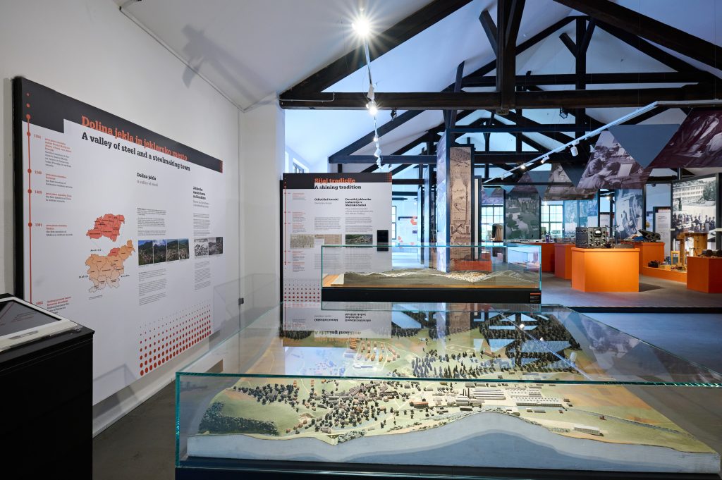 Exhibition space with maps, panels, and a central glass display case with exhibited objects related to ironworking heritage.