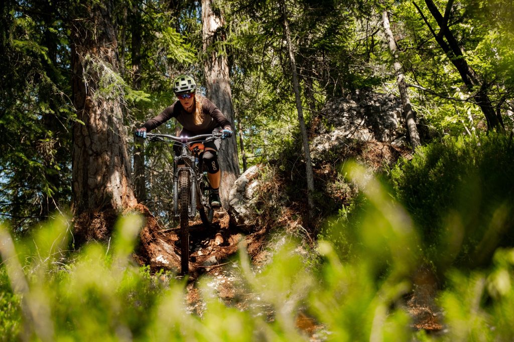 Female mountain biker descending a rugged forest path near Mežica.