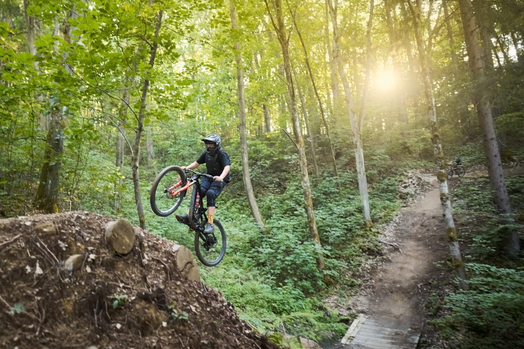 A mountain biker jumping on a rugged trail surrounded by Koroška forests.